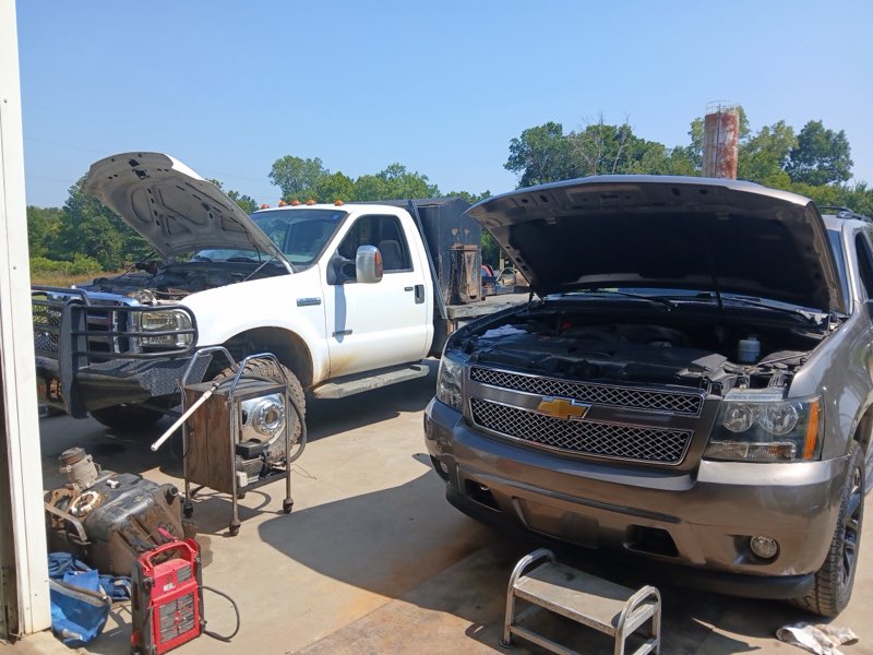 Two diesel trucks with hoods up being serviced outside the shop